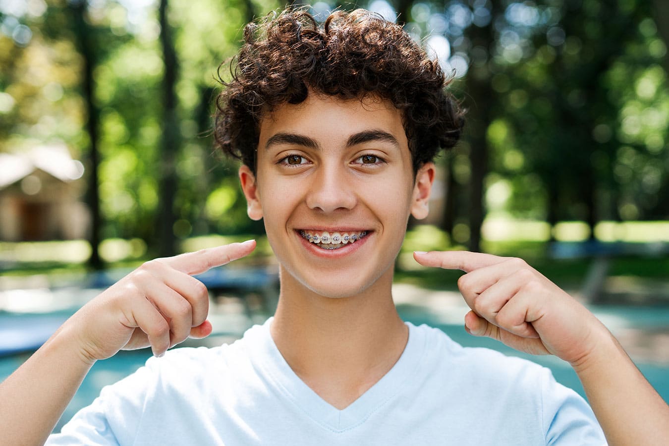 Smiling teenager pointing at his smile wearing braces